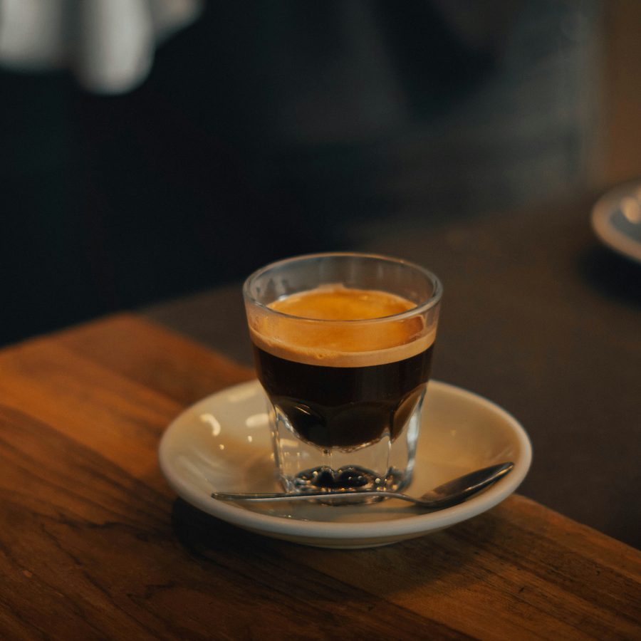 An espresso in a glass cup on a wooden bar counter